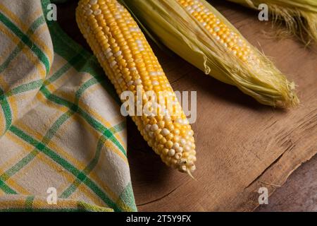 Vista ravvicinata di tre orecchie di mais dolce maturo con foglie verdi e asciugamano verde su fondo di legno vintage. Pannocchie con grani bianchi e gialli. Foto Stock