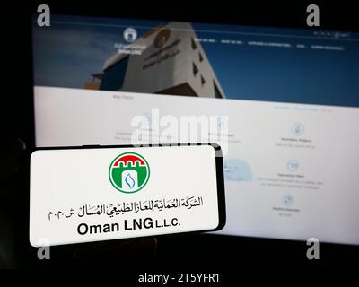 Persona che possiede uno smartphone con il logo della società di gas naturale liquefatto Oman Oman LNG davanti al sito web. Concentrarsi sul display del telefono. Foto Stock