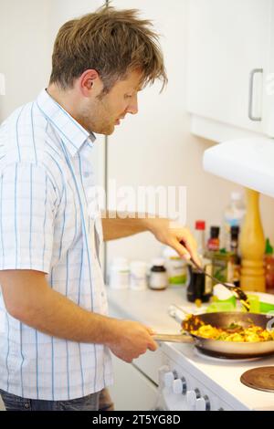 Uomo, stufa e friggi in cucina domestica di profilo per nutrizione, salute o preparazione in padella. Chef, cucina e cucchiaio con verdure per Foto Stock