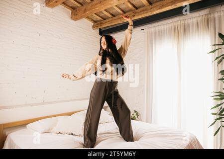 Giovane donna cinese che ascolta musica con le cuffie e balla su un letto. Foto Stock