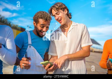 Sorridere e distrarre giovani multietnici che usano il telefono all'aperto accanto agli amici Foto Stock