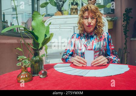 Vista frontale di una donna di tarocchi caucasici, seduta a casa, in sessione con la carta e guardando seriamente la macchina fotografica, persone e concetto di business, poliziotto Foto Stock
