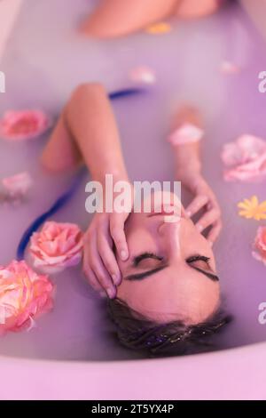 Ritratto artistico dall'alto di una donna morbida in un bagno con latte e fiori Foto Stock