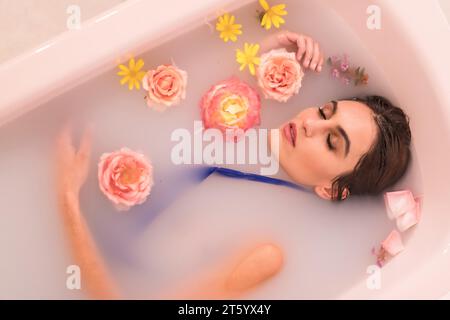 Ritratto artistico dall'alto di un modello che fa un bagno di latte con fiori Foto Stock