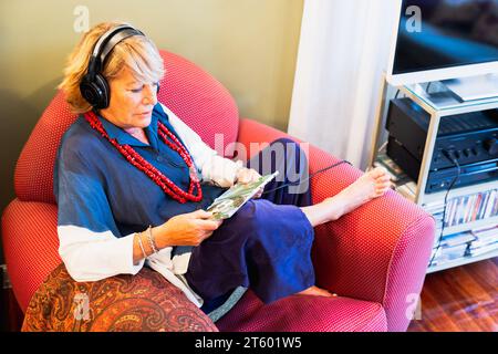 Donna matura felice che ascolta la musica comodamente seduto sul divano a casa Foto Stock