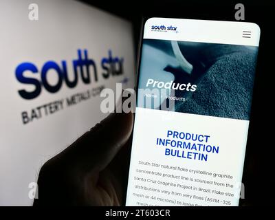 Persona che possiede uno smartphone con la pagina Web dell'azienda canadese South Star Battery Metals Corp. Davanti al logo. Concentrarsi sul centro del display del telefono. Foto Stock