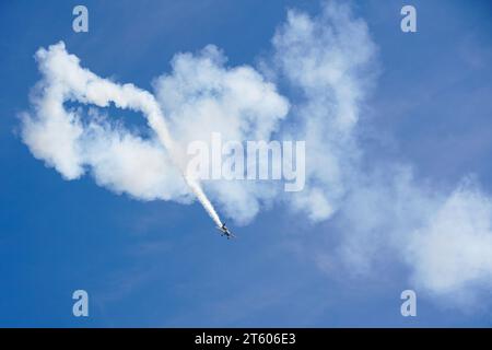 Liepaja, Lettonia- 06 agosto 2023: Aereo acrobatico che esegue una manovra acrobatica multipla lasciando una traccia di fumo su sfondo blu Foto Stock