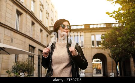 Elegante donna con occhiali da sole passeggia per City Street con zaino Foto Stock