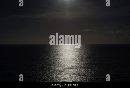 Il sole splendente lascia un sentiero di riflessi sul mare calmo. Foto Stock