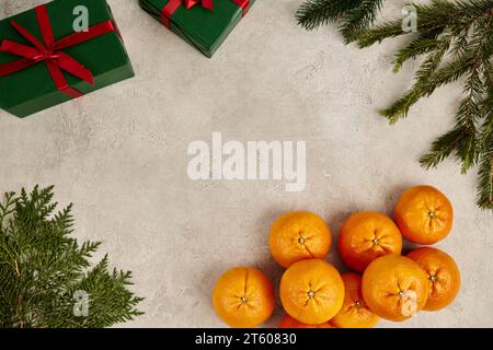 cornice con mandarini maturi e confezioni regalo verdi vicino a ginepro e brancini di pino su superficie ruvida Foto Stock