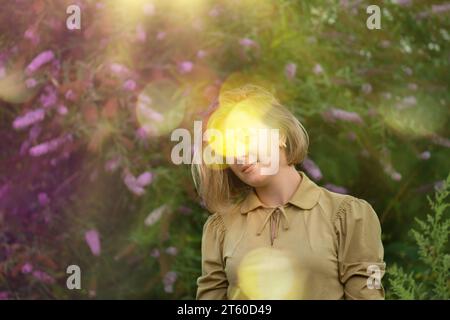 Donna romantica con un lungo abito dorato vintage che si posa su uno sfondo di fiori viola. Foto Stock