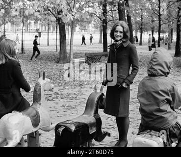 Anni '1960, la modella donna guarda i bambini che giocano su una giostra a cavallo, il giardino Jardin des Tuileries, Parigi, Francia, Europa, Foto Stock