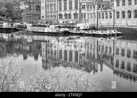 Edifici storici e file di barche si riflettono in un fiume. I detriti di alberi di una recente tempesta galleggiano vicino a una barca turistica. Foto Stock