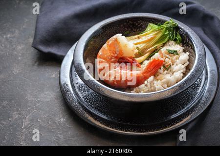 Gamberi giganti fritti o gamberi con riso e pak choi in una ciotola di ceramica nera maculata su sfondo scuro, cucina in stile asiatico, spazio copia, selezione Foto Stock