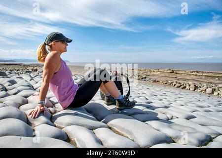 Donna sulla spiaggia di Kilve e sulla costa rocciosa, a Kilve, Quantocks, Somerset, Regno Unito in una giornata di sole. La spiaggia è famosa per aver trovato fossili. Foto Stock