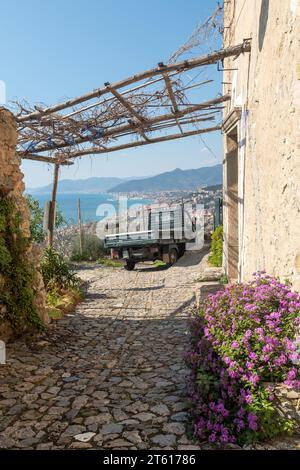 Auto Piaggio Ape parcheggiata di fronte a una vecchia casa in pietra con una splendida vista sulla Riviera delle Palme in primavera, Borgio Verezzi, Savona, Liguria, Italia Foto Stock