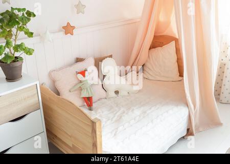 grande camera da letto luminosa con pareti bianche e un grande letto con copriletto in maglia bianca. vicino al letto c'è una piccola culla in vimini con un giocattolo Foto Stock