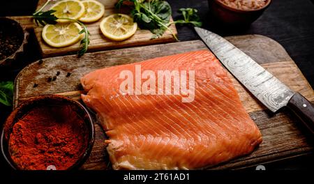 Filetto di salmone crudo con coltello, spezie e limoni su tavola di legno. Pesce omega rosso sano e basilico verde in cucina Foto Stock