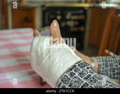 donna anziana con un polso gettato che guarda un telefono cellulare a casa Foto Stock