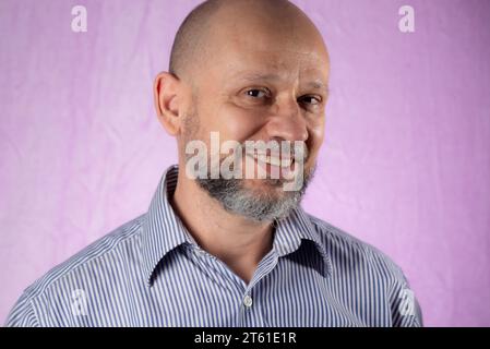 Uomo barbuto, calvo e amichevole sorridente davanti alla fotocamera su sfondo rosa. Foto Stock