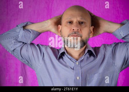 Uomo calvo e barbuto che guarda la fotocamera su sfondo rosa. Foto Stock