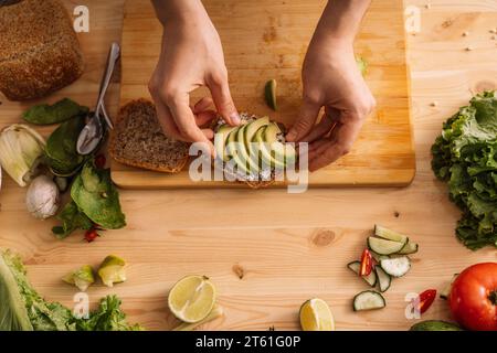 Signora che prepara un panino vegetariano su un tavolo di legno tra verdure fresche Foto Stock