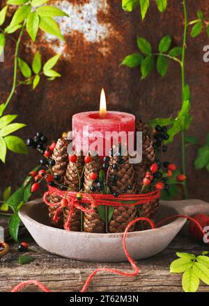 Candela rossa di Natale decorata con pineconi, fianchi rosa e bacche di privet nero, lana di iuta. Decorazioni fatte a mano. Messa a fuoco selettiva. Foto Stock