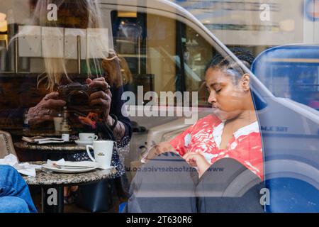 Una giovane donna vista dalla finestra di un bar a Oxford, Inghilterra, Regno Unito. Il fotografo viene riflesso nella finestra Foto Stock