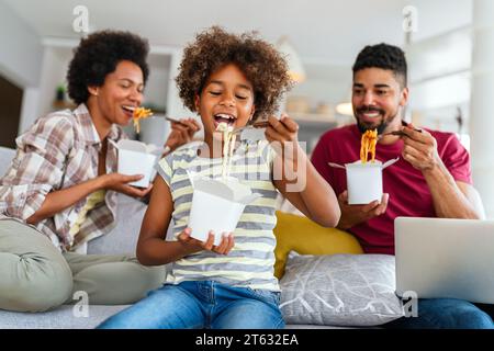 Felice famiglia africana che mangia in salotto e si diverte a trascorrere del tempo insieme. Piatti da asporto casalinghi Foto Stock