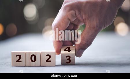 2024 Happy New Year eve blocchi di legno flip change mano sfondo blu. Conto alla rovescia a partire dalla fine del calendario delle azioni 2023 strategia visione futura Foto Stock