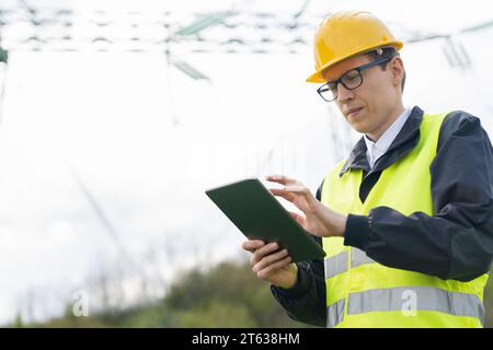 Progettare con un tablet digitale sullo sfondo di una torre della linea elettrica. Foto Stock