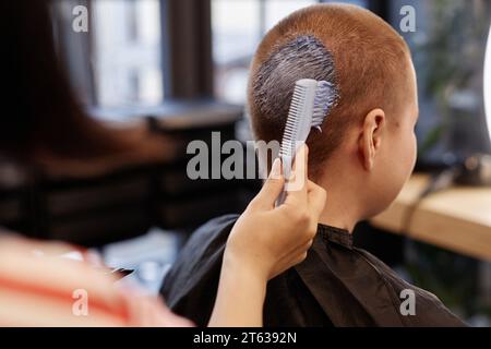 Primo piano di una parrucchiera femminile che applica candeggina ai capelli corti di una giovane donna in un salone di bellezza, una sessione professionale di colorazione dei capelli Foto Stock
