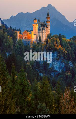 Castello di Neuschwanstein illuminato dopo il tramonto circondato da colori autunnali, situato vicino alla città di Füssen, nel Allgäu, in Baviera, a sud Foto Stock