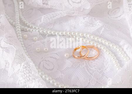 Due fedi nuziali dorati si trovano su una lussuosa parte vintage dell'abito da sposa della sposa con una serie di perle. Concetto di matrimonio Foto Stock