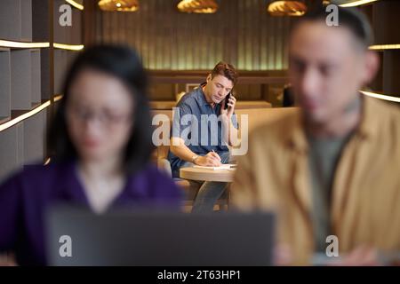 Imprenditore di mezza età che telefona al partner commerciale e scrive idee Foto Stock