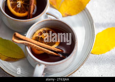 composto da due tazze di tè aromatico speziato con bastoncini di cannella, anice e fette di arancia secche circondate da splendenti foglie gialle autunnali su un textur Foto Stock