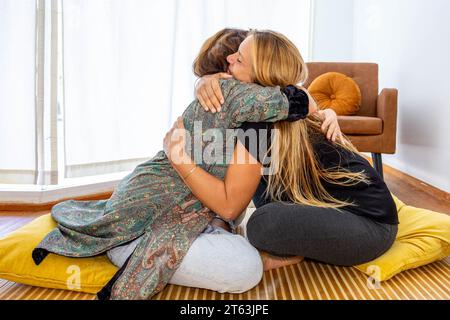 Due donne sedute su un divano mentre si abbracciano in una riunione di supporto emotivo e psicologico Foto Stock