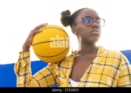 Donna afroamericana premurosa che tiene il basket mentre si trova in piedi contro il cielo limpido durante la giornata di sole Foto Stock