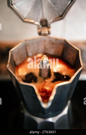 Primo piano del caffè bollente in una macchina per caffè espresso con piano cottura aperto che cattura il ricco aroma e la consistenza del caffè italiano appena fatto in un setti casalingo Foto Stock