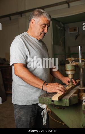 Vista laterale uomo anziano che lavora diligentemente su un pezzo di legno utilizzando macchinari in un'officina di falegnameria a Toledo Foto Stock