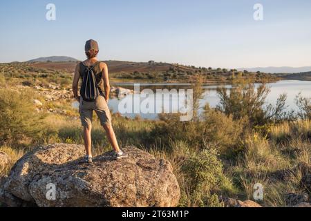 Vista posteriore di una donna irriconoscibile con cappello e zaino in cima a una roccia che si affaccia sul Pantano de Layos, Toledo, Spagna Foto Stock