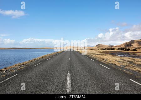 Prospettiva in diminuzione di asfalto strada vuota con segnaletica stradale che passa attraverso il lago panoramico contro il cielo in Islanda Foto Stock