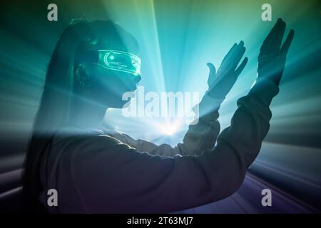 Vista laterale di una giovane donna che indossa futuristici occhiali LED VR braccia mobili luci proiettate mentre esplora il cyberspazio in studio Foto Stock