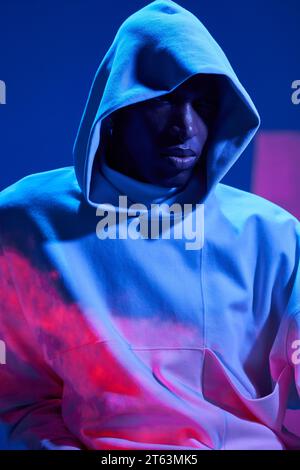 Ritratto di un giovane afro-americano vestito con una giacca con cappuccio che guarda lontano seriamente in studio con luci illuminate Foto Stock