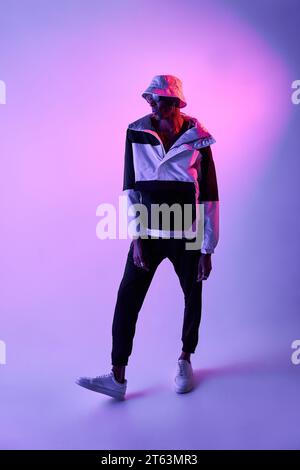 Corpo completo di un giovane afroamericano con eleganti occhiali da sole e cappello in piedi e in posa con sicurezza sulla luce luminosa dello studio Foto Stock
