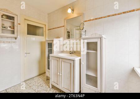 Specchio su lavabo d'epoca con armadi di legno vuoti in una cucina in stile country con pareti bianche a casa Foto Stock