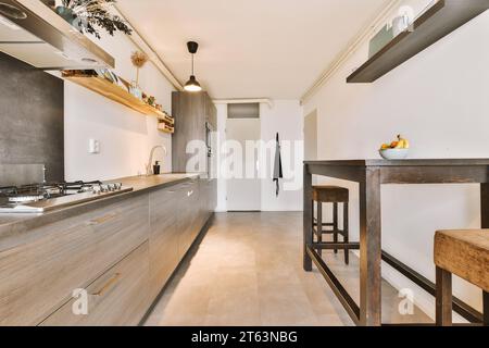 Capanna sulla stufa sul piano di lavoro in legno nella moderna cucina dell'appartamento contemporaneo con tavolo e sgabelli Foto Stock