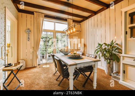 Tavolo da pranzo e sedie sotto le luci pendenti illuminate del soggiorno con finestre luminose in una casa moderna Foto Stock