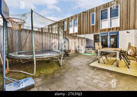 Trampolino e sedia a dondolo con tavolo da pranzo e sedie nel patio sul retro della casa moderna durante il giorno di sole Foto Stock