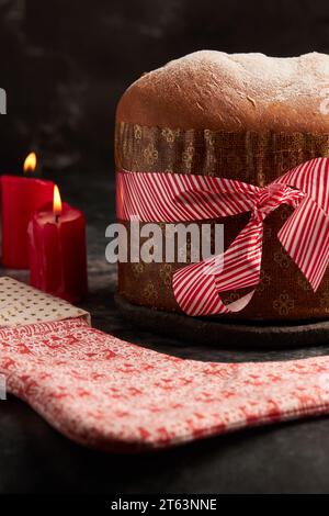 Un panettone ben presentato avvolto da un nastro rosso a righe, accompagnato da un tessuto decorativo con motivi festivi, inserito in un ambiente accogliente Foto Stock